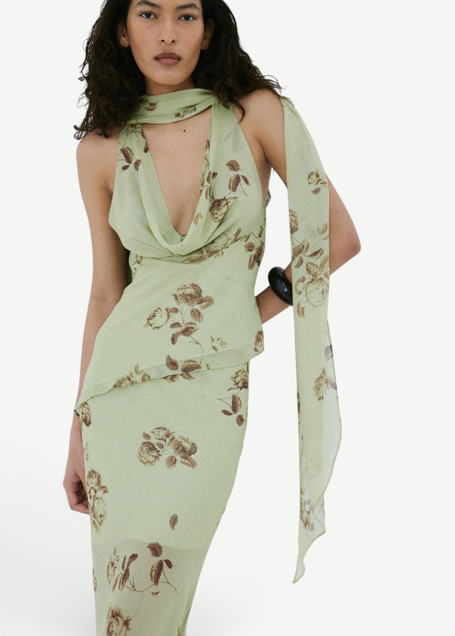 A person wears a pale green, floral-print bohemian style Diosa Top with a matching scarf and an asymmetrical hemline.