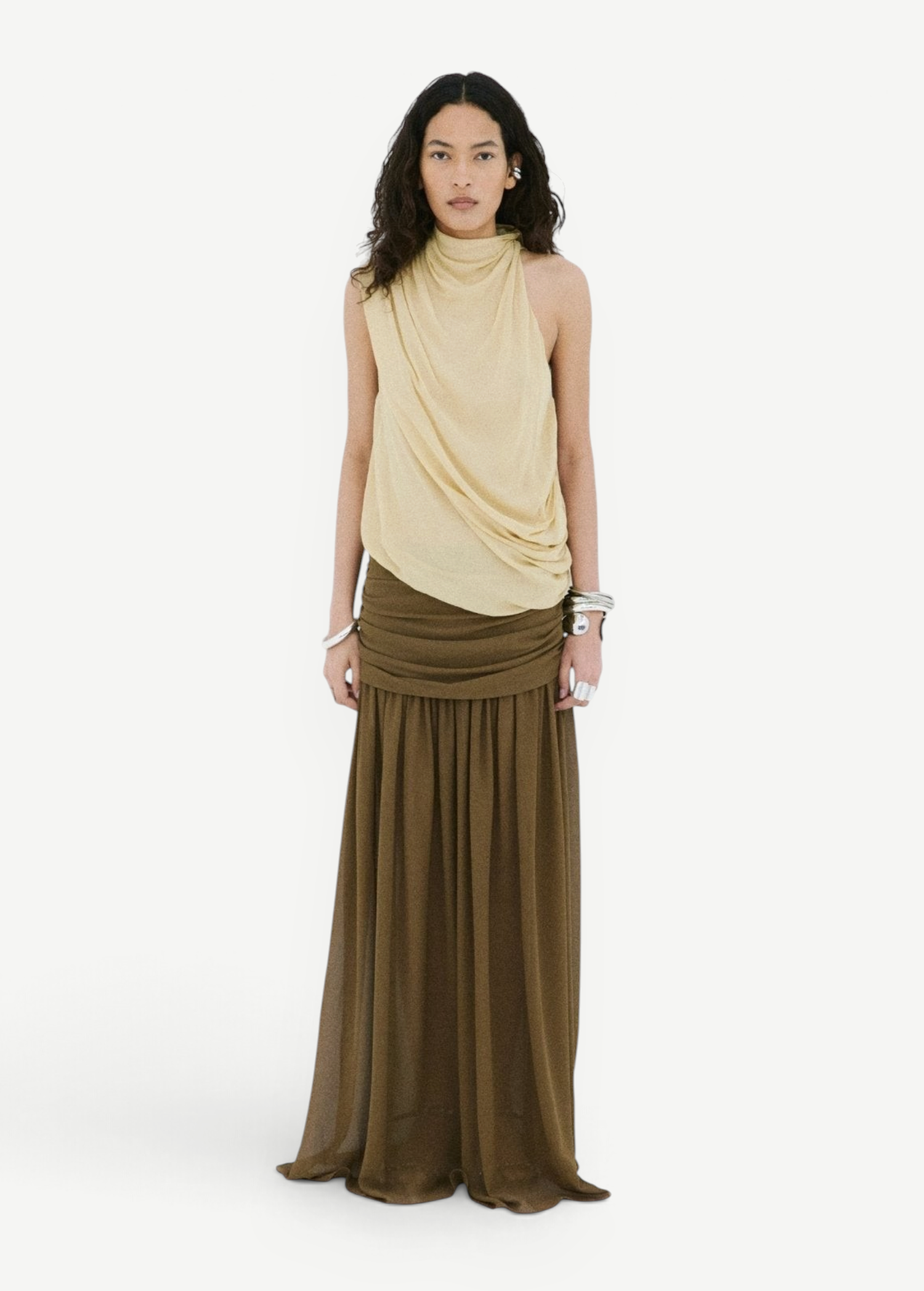 A person wears a beige sleeveless draped top and an Agapito Skirt in dark olive taupe chiffon, creating an elongated silhouette.