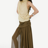 A person poses against a white wall wearing a pale yellow sleeveless top and an olive green Agapito Skirt that creates an elongated, floor-length chiffon silhouette.