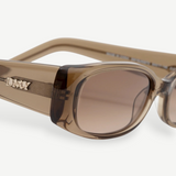 Close-up of the Billy sunglasses, showcasing a thick, rectangular frame in brown crafted from premium Mazzucchelli cellulose acetate. The metallic DMY logo adorns the temple, while the tinted lenses offer UV protection. Set against a plain white background.