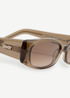 Close-up of the Billy sunglasses, showcasing a thick, rectangular frame in brown crafted from premium Mazzucchelli cellulose acetate. The metallic DMY logo adorns the temple, while the tinted lenses offer UV protection. Set against a plain white background.