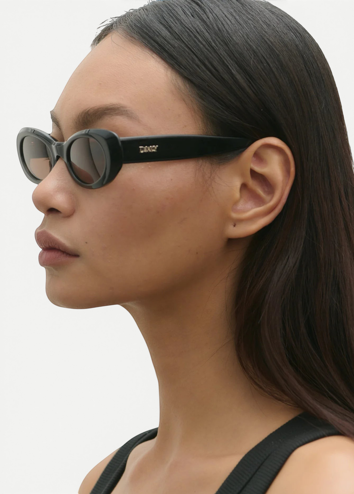 Model wearing KABE SHOP INC Naomi oval black Italian acetate sunglasses in a profile view against a white background.