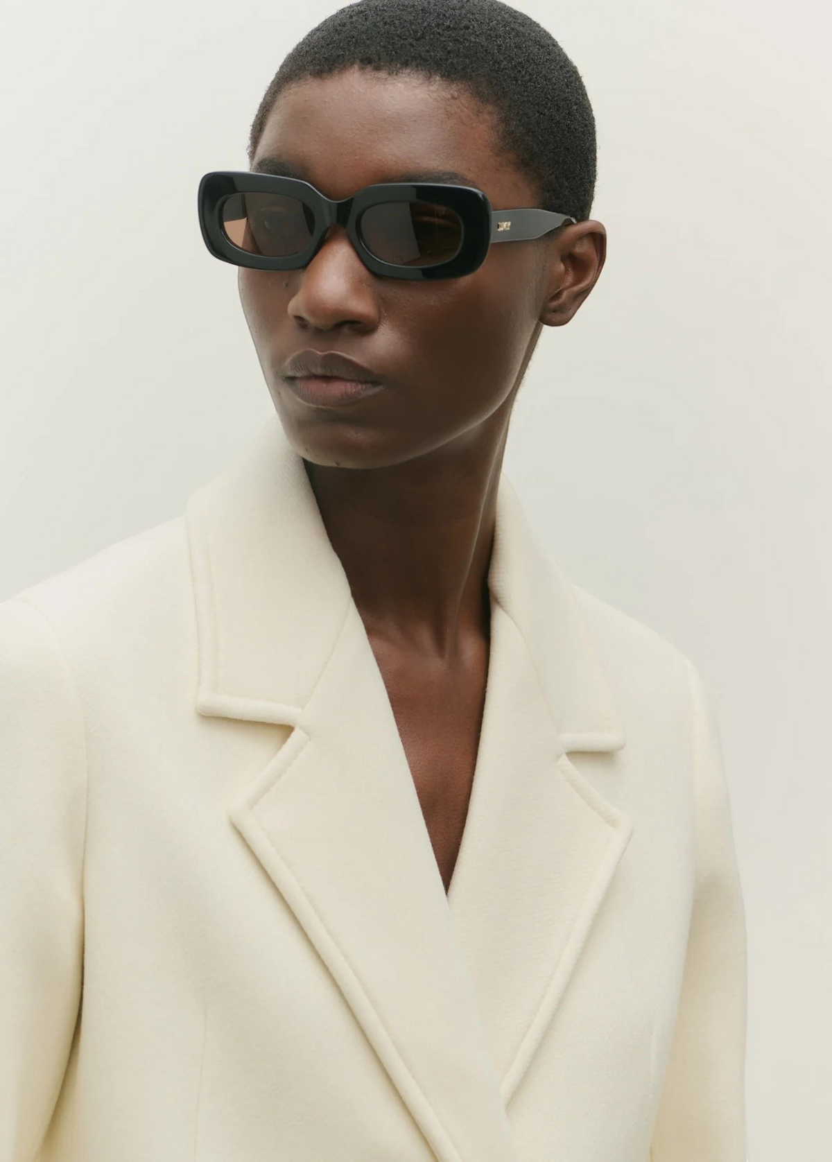 Model wearing KABE SHOP INC Vivian black rectangular acetate sunglasses with a cream wool blazer