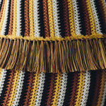 Close-up of the Misti Sleeveless Top featuring vertical stripes in yellow, brown, white, and black with a wide, artisanal fringe trim across the midsection.