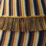 Close-up of the Misti Sleeveless Top featuring vertical stripes in yellow, brown, white, and black with a wide, artisanal fringe trim across the midsection.