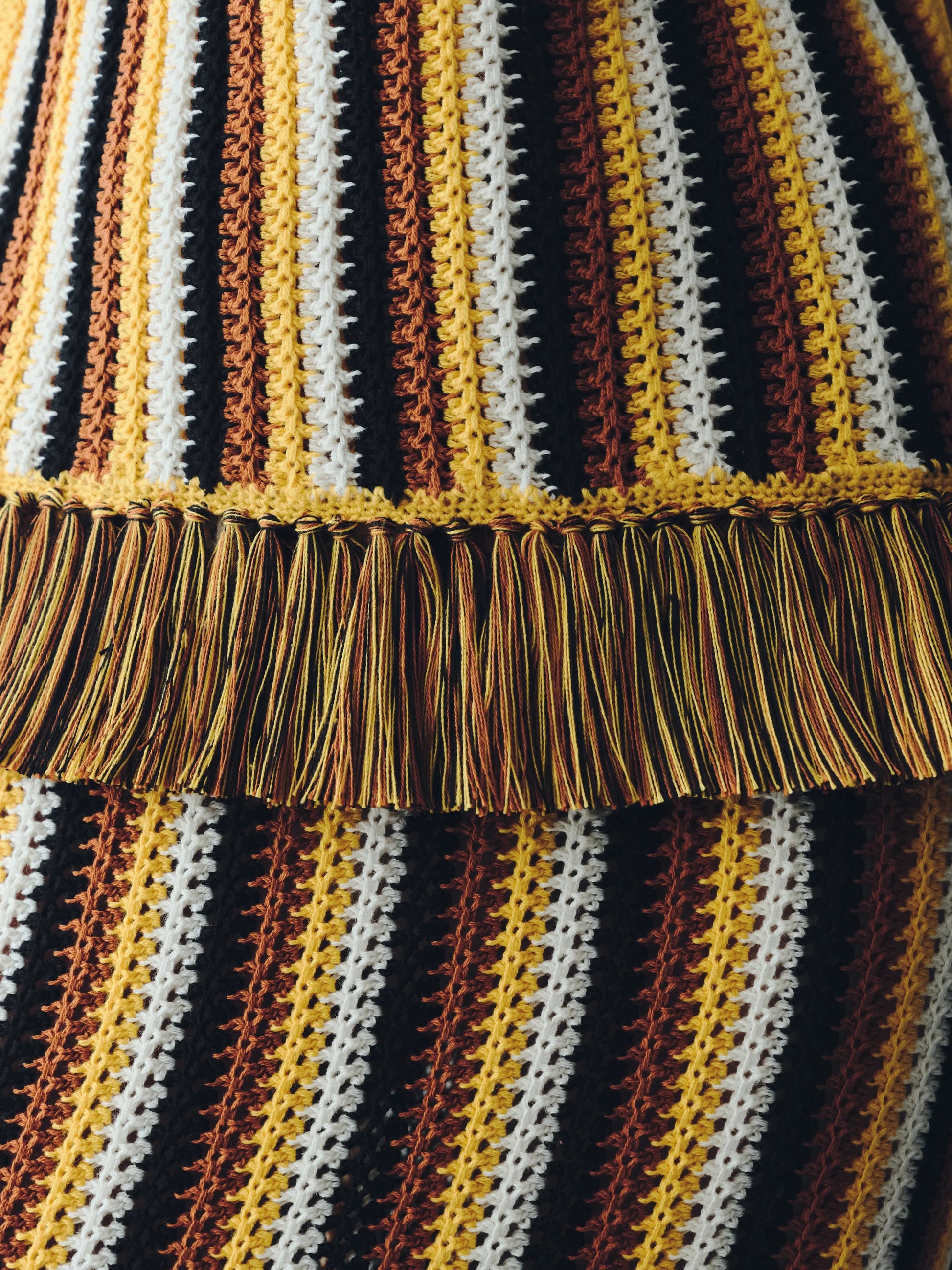 Close-up of the Misti Sleeveless Top featuring vertical stripes in yellow, brown, white, and black with a wide, artisanal fringe trim across the midsection.