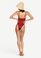 Model wearing a KABE SHOP INC The Orb red minimalist one-piece swimsuit with thin straps and a straw sun hat