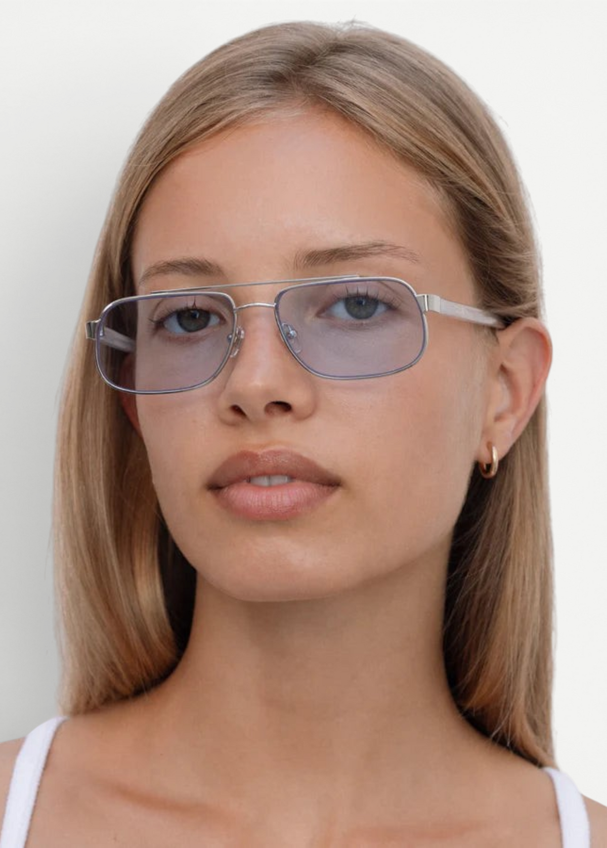 A person with straight blonde hair wears the Evangeline stainless steel frame, blue-tinted rectangular sunglasses and a white top, looking at the camera against a plain white background.
