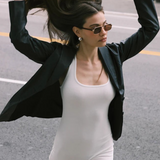 Wearing the Evangeline aviator sunglasses with a stainless steel frame, a woman in a black blazer and white romper flips her long hair with both hands while walking on a city street.