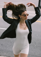Wearing the Evangeline aviator sunglasses with a stainless steel frame, a woman in a black blazer and white romper flips her long hair with both hands while walking on a city street.