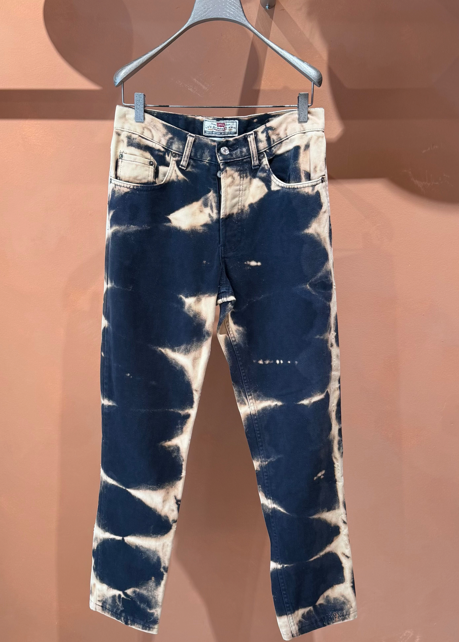 KABE SHOP INC tie dye denim jeans with a dark blue and bleached white abstract pattern hanging on a clothes hanger.