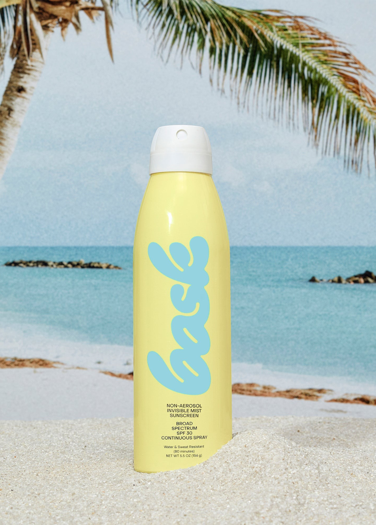 KABE SHOP INC yellow continuous spray sunscreen bottle on sandy beach with palm tree and ocean background