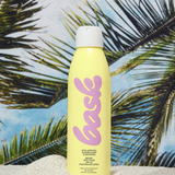 KABE SHOP INC yellow aerosol sunscreen spray bottle standing in white sand against a tropical palm tree background.