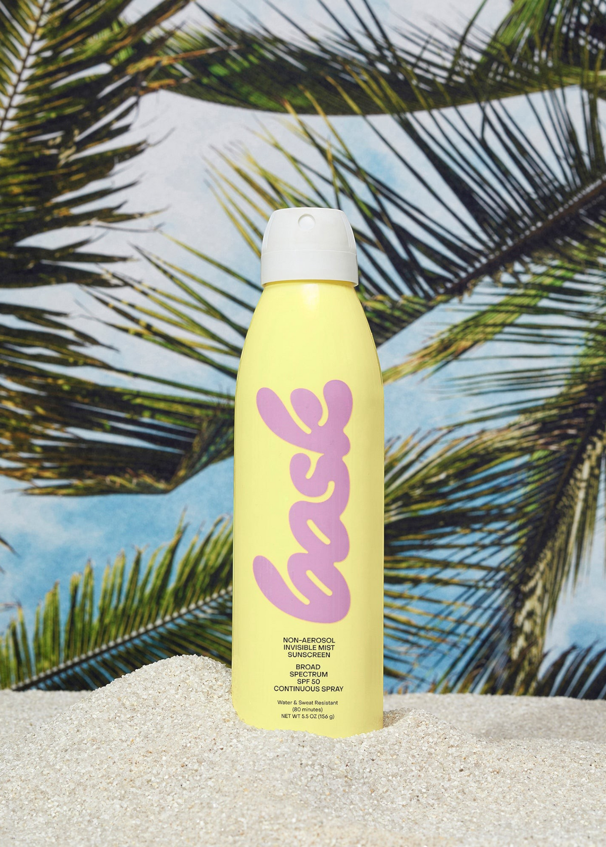 KABE SHOP INC yellow aerosol sunscreen spray bottle standing in white sand against a tropical palm tree background.