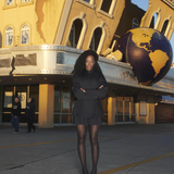 A model wearing KABE SHOP INC black tailored boxer shorts with a matching jacket and sheer tights outdoors.