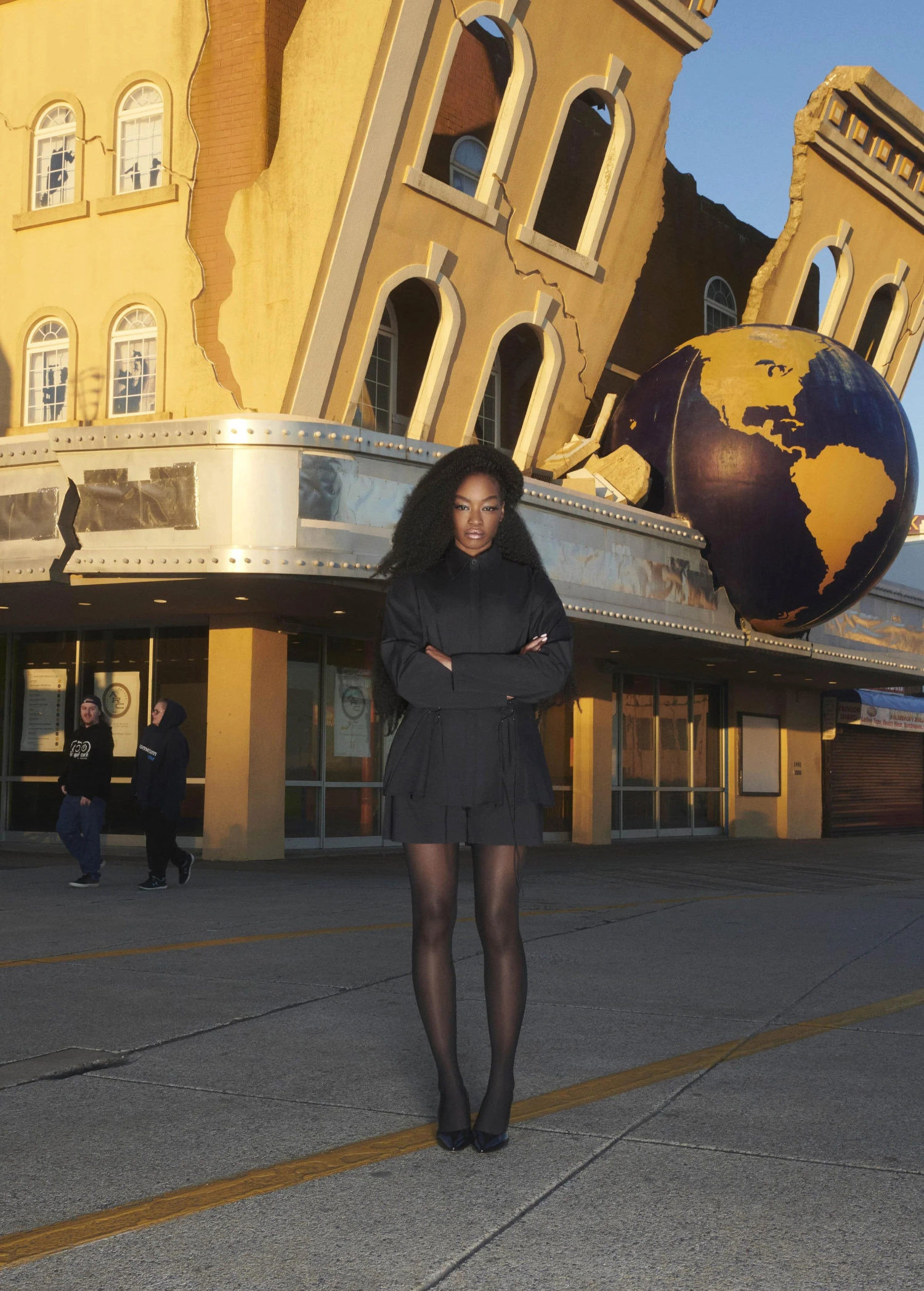 A model wearing KABE SHOP INC black tailored boxer shorts with a matching jacket and sheer tights outdoors.