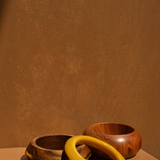KABE SHOP INC set of three sculptural bangles featuring natural wood and smooth yellow resin on a tan background.