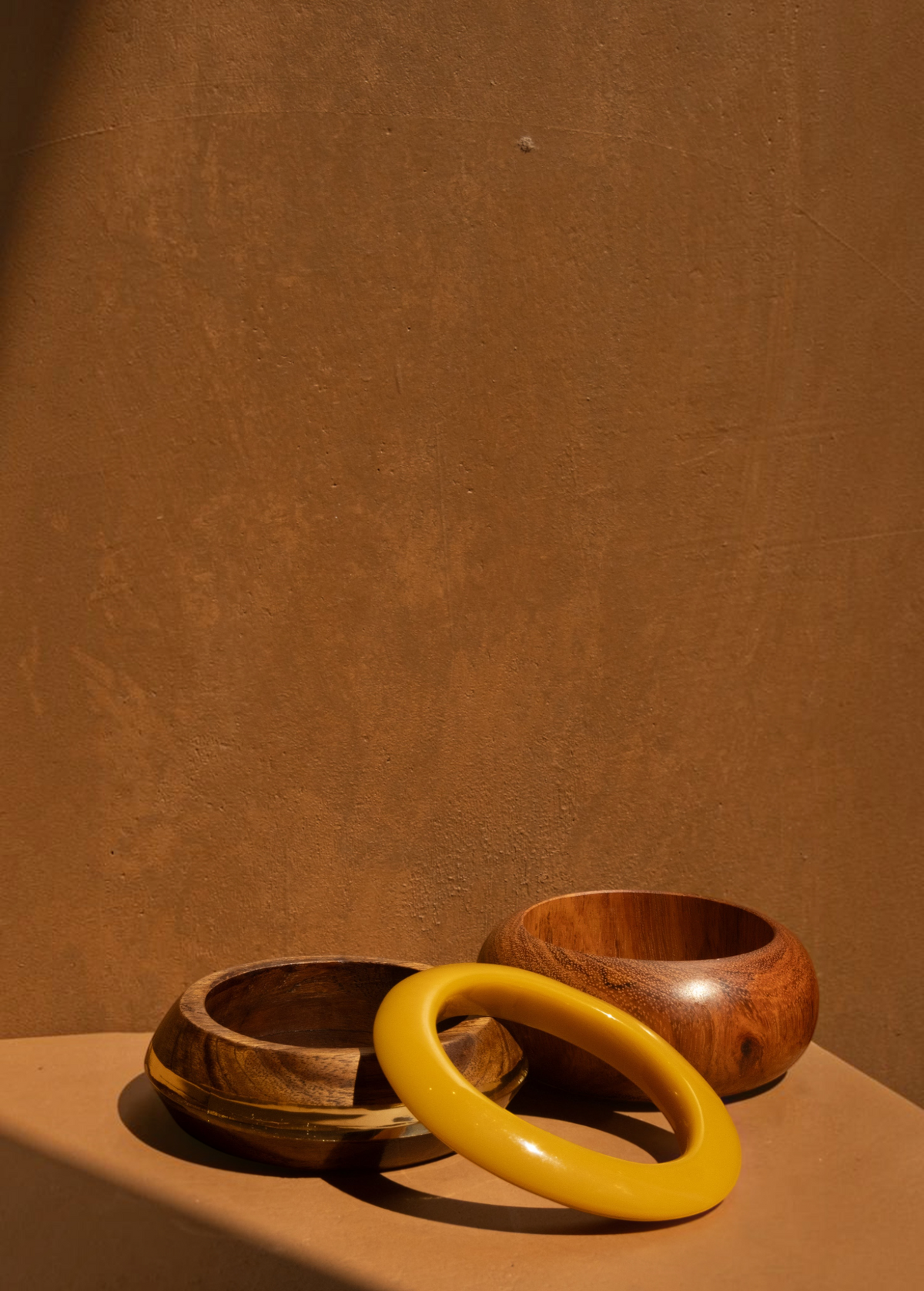 KABE SHOP INC set of three sculptural bangles featuring natural wood and smooth yellow resin on a tan background.