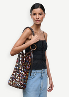 Model wearing a KABE SHOP INC Del Mar bucket bag featuring a multi-colored beaded net design with brown leather handles.