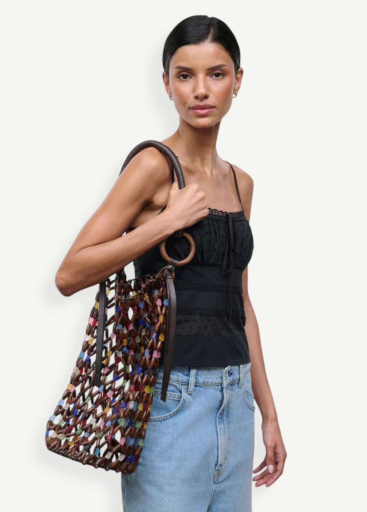Model wearing a KABE SHOP INC Del Mar bucket bag featuring a multi-colored beaded net design with brown leather handles.