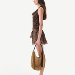 Woman in the Hunni Top—a brown polka dot sleeveless top with a cowl neckline—paired with a short floral skirt, beige cap, and loafers, stands in profile holding a tan hobo bag with tassels against a white background.