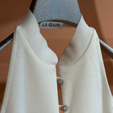 Modjolokia Flowers Top, a white sleeveless shirt with a high collar and two jewel-like floral clasps at the neckline.