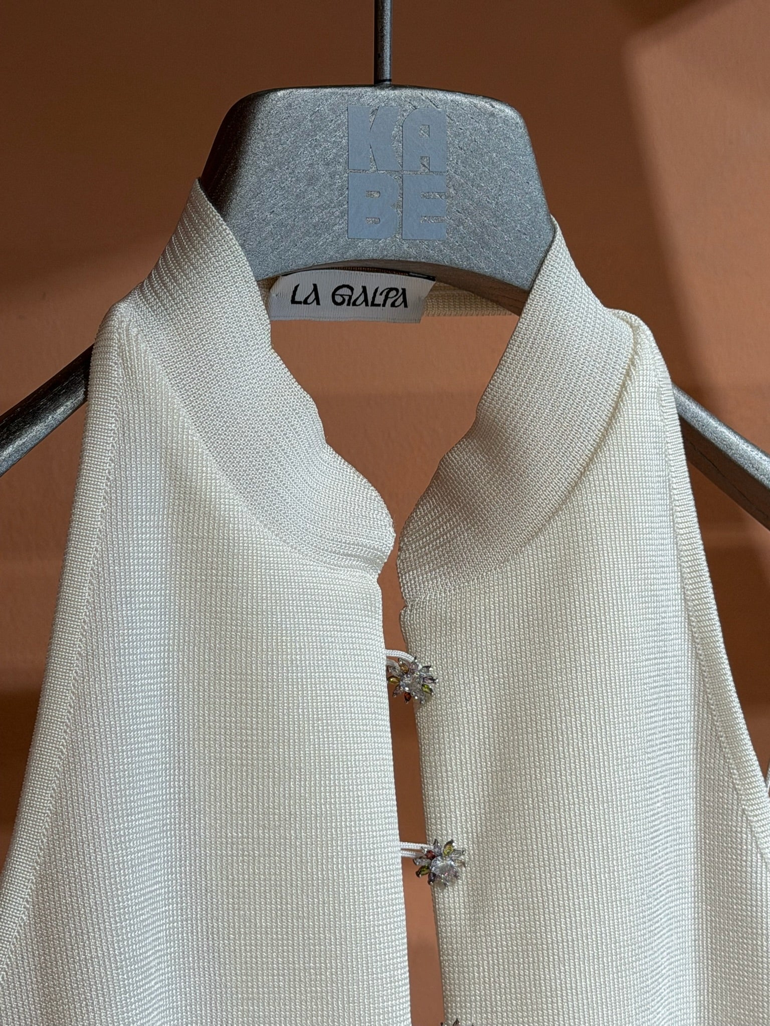 Modjolokia Flowers Top, a white sleeveless shirt with a high collar and two jewel-like floral clasps at the neckline.