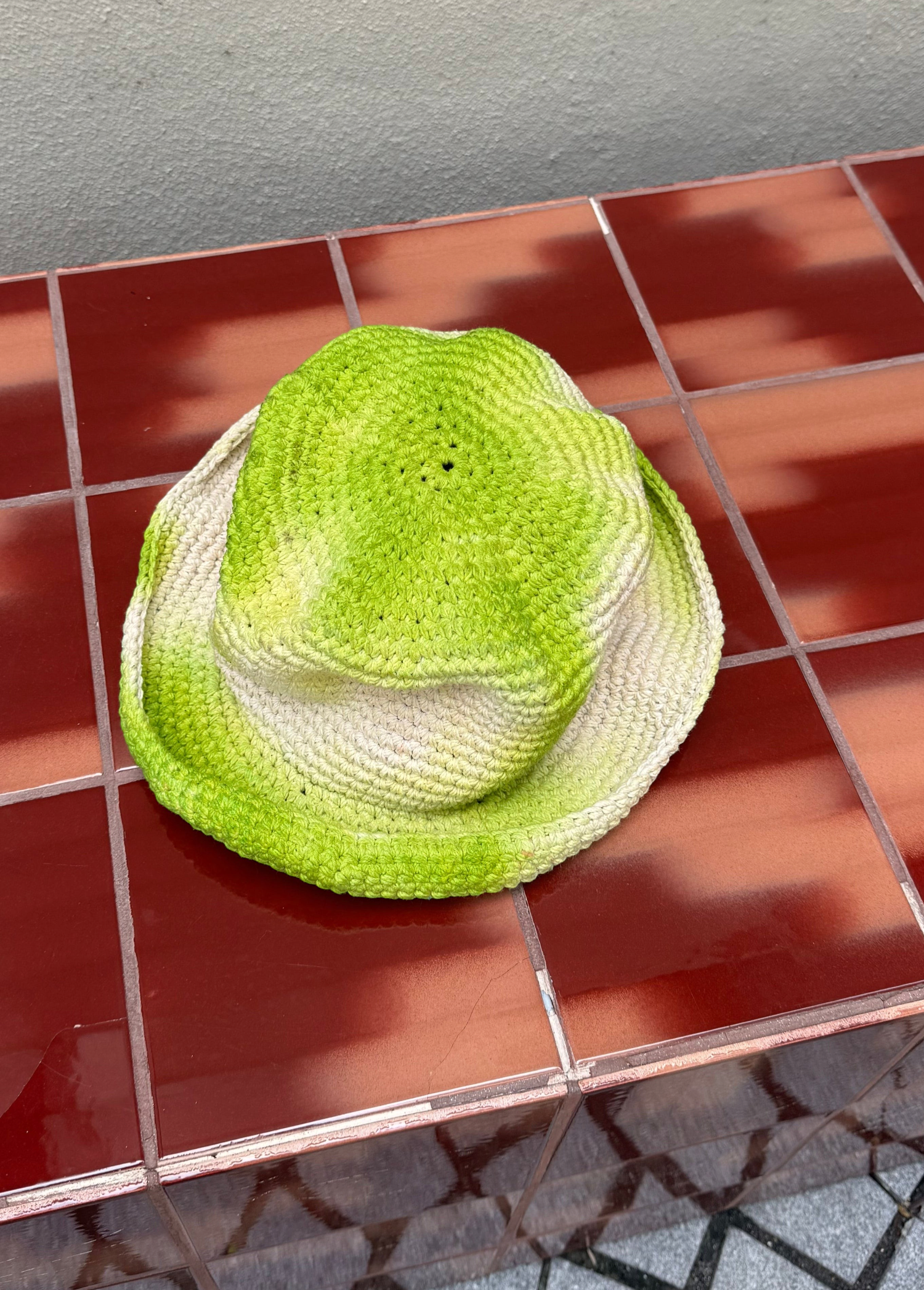 KABE SHOP INC handmade crochet bucket hat with a vibrant green and white tie-dye pattern on a red tiled surface