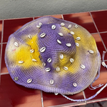 KABE SHOP INC crochet tie-dye hat in purple and yellow with decorative white seashells and a braided chin strap.
