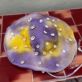 KABE SHOP INC crochet tie-dye hat in purple and yellow with decorative white seashells and a braided chin strap.