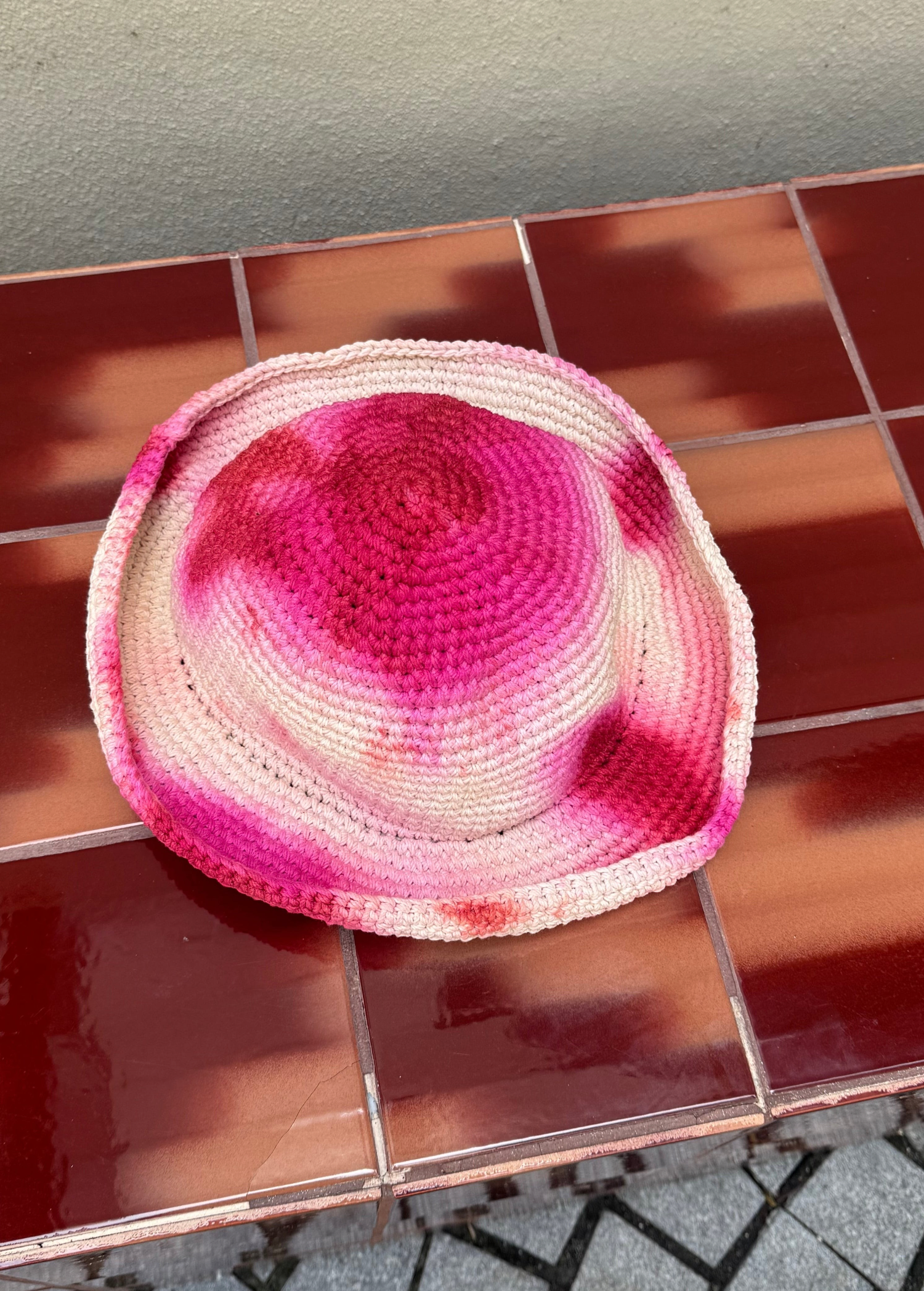 KABE SHOP INC handmade crochet bucket hat featuring a vibrant pink and white tie-dye pattern on a tiled surface.