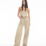 A woman with long dark hair wears a beige, asymmetrical sleeveless top and Cold Dye Boyfriend Jeans with Patch Pockets. She stands confidently against a plain white background, with one hand in her patch pocket and the other by her side.