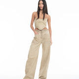 A woman with long dark hair wears a beige, asymmetrical sleeveless top and Cold Dye Boyfriend Jeans with Patch Pockets. She stands confidently against a plain white background, with one hand in her patch pocket and the other by her side.
