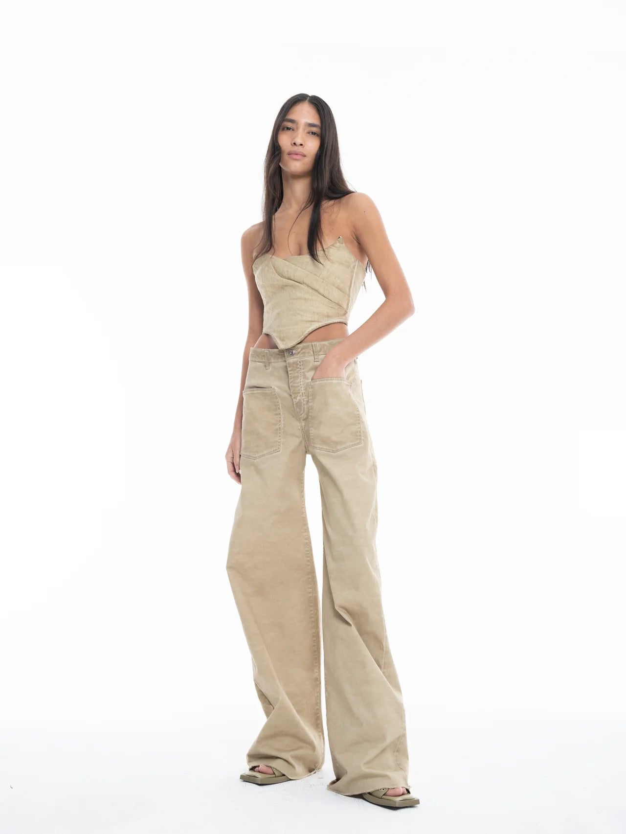 A woman stands against a white background, wearing Cold Dye Boyfriend Jeans with patch pockets, styled with a beige strapless top and green sandals. She has long, straight hair and her hands rest casually in her pockets.