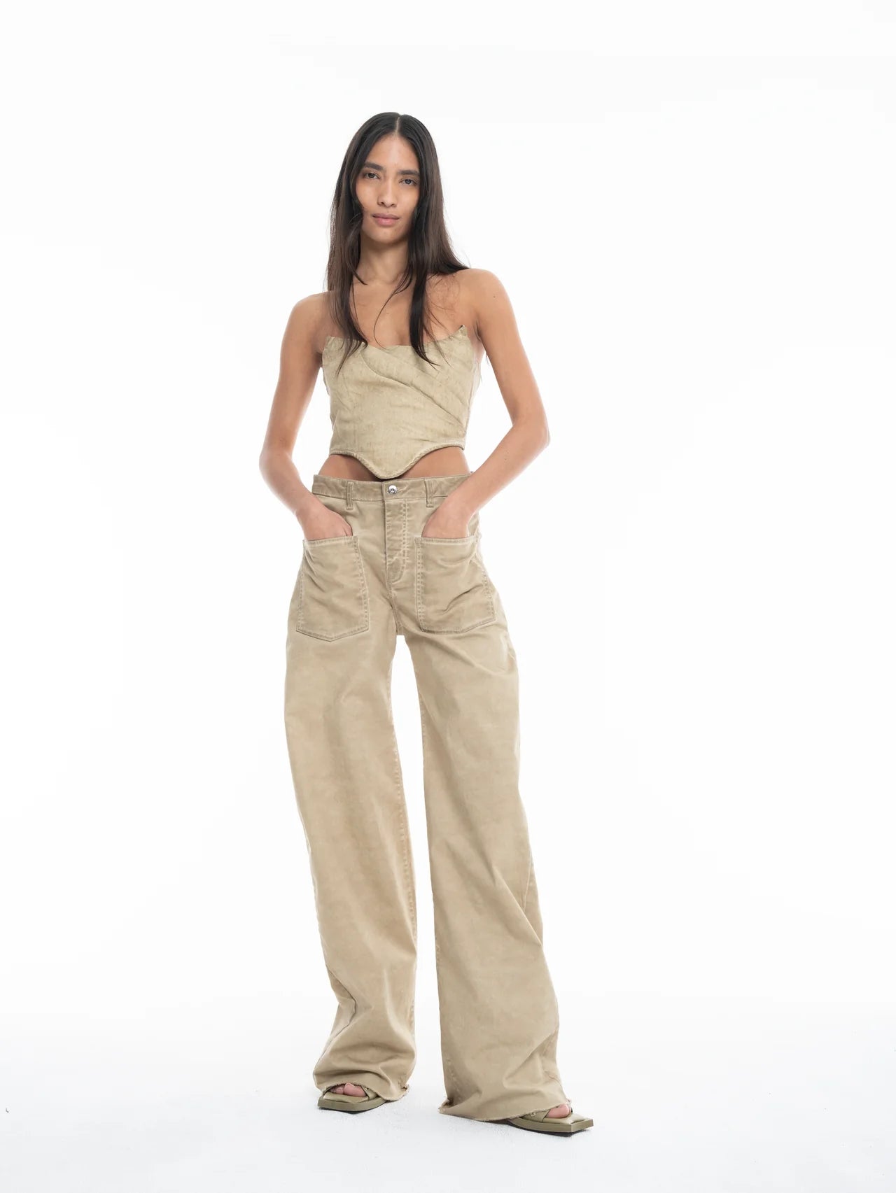 A woman stands against a white background, wearing a beige strapless top and Cold Dye Boyfriend Jeans with Patch Pockets featuring visible pockets and wide legs. She has long straight hair and her hands are tucked into her pockets.