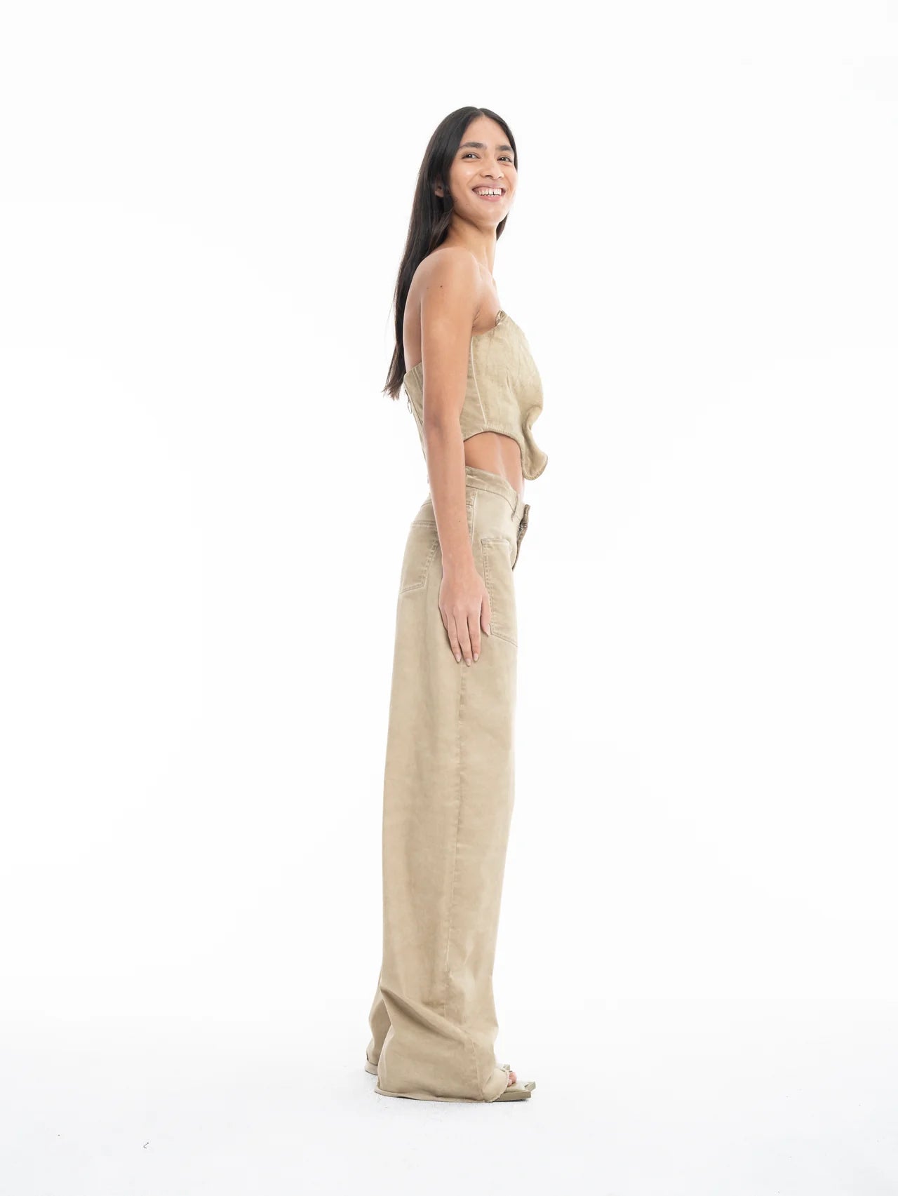 A woman stands sideways and smiles, wearing a beige sleeveless top paired with Cold Dye Boyfriend Jeans with Patch Pockets in a matching high-waisted, wide-leg style against a white background.