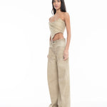 A woman with long hair wears a tan, asymmetrical strapless top and Cold Dye Boyfriend Jeans with Patch Pockets, which feature wide legs and a stylish patch pocket. She stands facing slightly left against a plain white background.