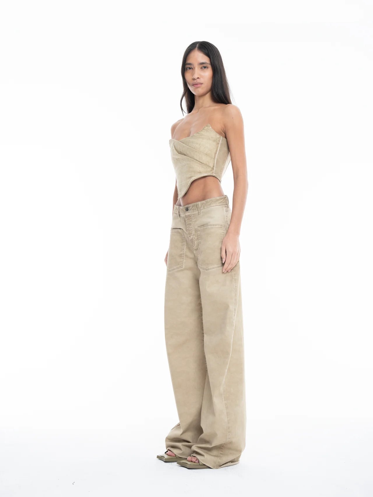 A woman with long hair wears a tan, asymmetrical strapless top and Cold Dye Boyfriend Jeans with Patch Pockets, which feature wide legs and a stylish patch pocket. She stands facing slightly left against a plain white background.