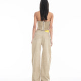 A woman stands facing away against a plain white background, wearing a strapless beige corset top and the Cold Dye Boyfriend Jeans with Patch Pockets, featuring a loose, wide-leg khaki design and a yellow tag visible in the back patch pocket.