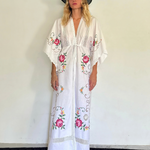 KABE SHOP INC white kaftan dress with floral embroidery, lace trim, and v-neck worn by a woman in a black hat