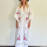 KABE SHOP INC white kaftan dress with floral embroidery, lace trim, and v-neck worn by a woman in a black hat
