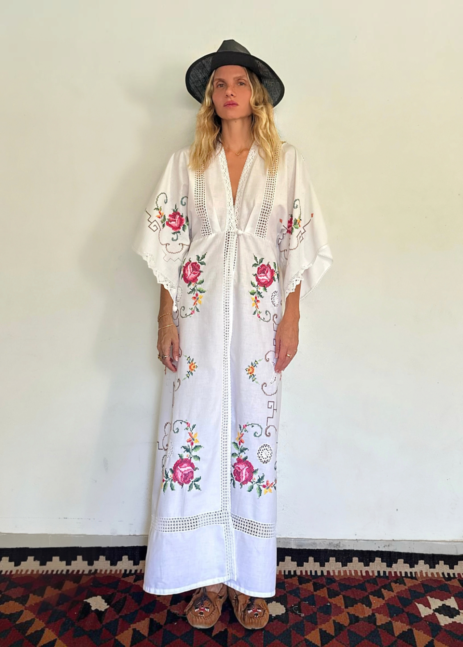 KABE SHOP INC white kaftan dress with floral embroidery, lace trim, and v-neck worn by a woman in a black hat