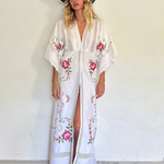 KABE SHOP INC white kaftan dress with floral embroidery, deep V-neck, and lace trim worn by a model in a hat