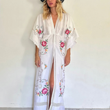 KABE SHOP INC white kaftan dress with floral embroidery, deep V-neck, and lace trim worn by a model in a hat