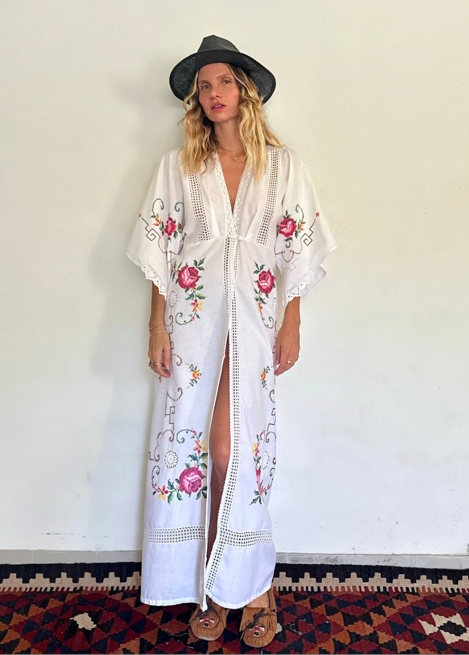 KABE SHOP INC white kaftan dress with floral embroidery, deep V-neck, and lace trim worn by a model in a hat