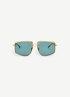 The Miranda Sunglasses feature an oversized, geometric frame expertly crafted from Japanese titanium with a luxurious gold-plated finish and distinctive blue-green tinted lenses, shown facing forward against a plain white background.