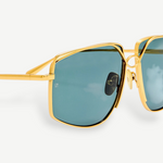 Close-up of the Miranda Sunglasses, featuring an oversized frame with gold-plated metal accents and green-tinted square lenses, shown against a plain white background.