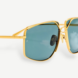 Close-up of the Miranda Sunglasses, featuring an oversized frame with gold-plated metal accents and green-tinted square lenses, shown against a plain white background.