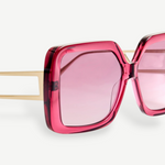 Close-up of the Macy Sunglasses, showcasing oversized square frames crafted from bold pink Italian acetate, with pink tinted lenses and gold plated temples set against a plain white background.
