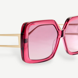 Close-up of the Macy Sunglasses, showcasing oversized square frames crafted from bold pink Italian acetate, with pink tinted lenses and gold plated temples set against a plain white background.